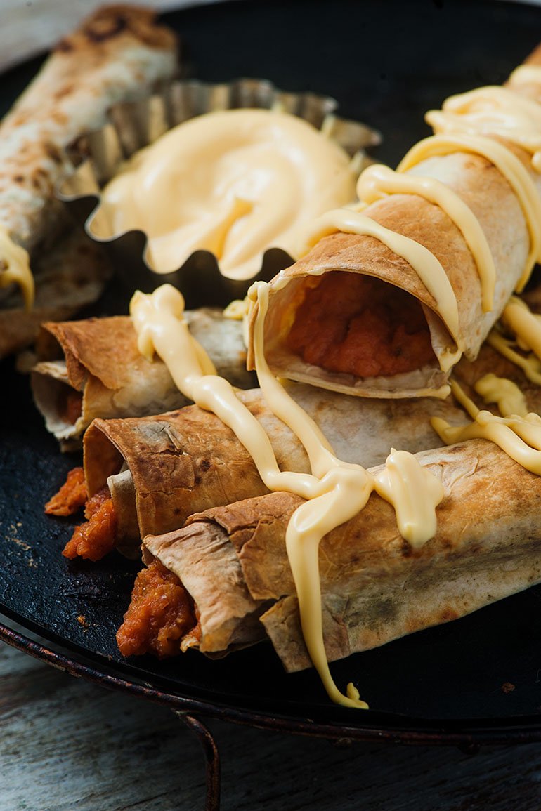 vegan baked buffalo chickpea taquitos with vegan cheese sauce