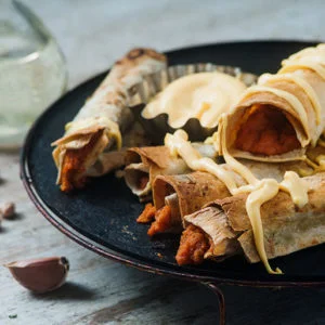 vegan baked buffalo chickpea taquitos with vegan cheese sauce served on plate