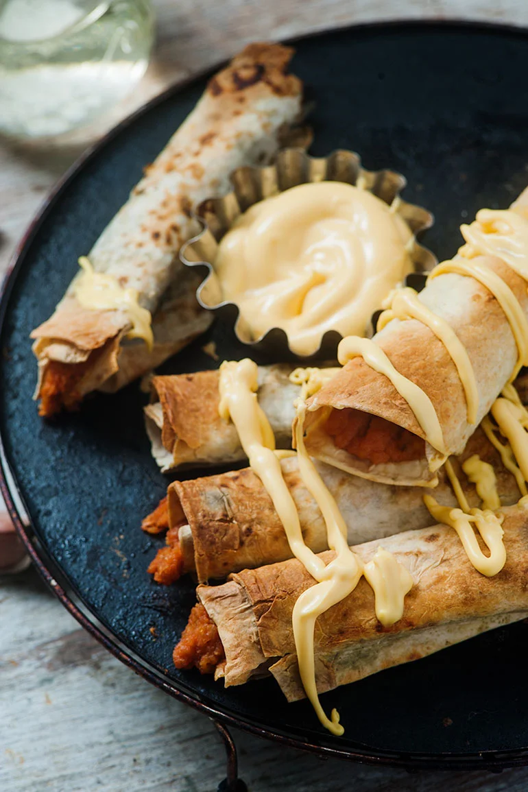 vegan baked buffalo chickpea taquitos with vegan cheese sauce