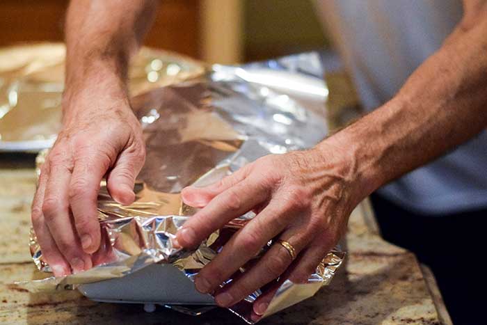 Hands covering casserole dish with aluminum foil to back in oven