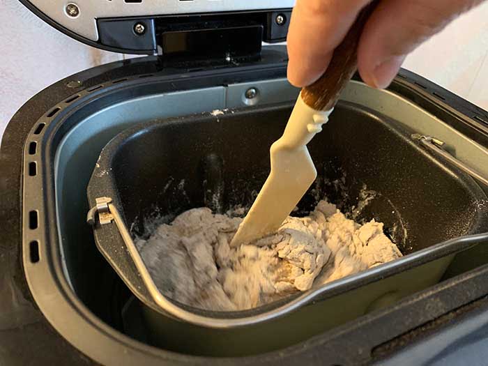 Home bread maker machine. Hand is mixing the paste.