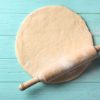Rolling pin with dough on wooden background