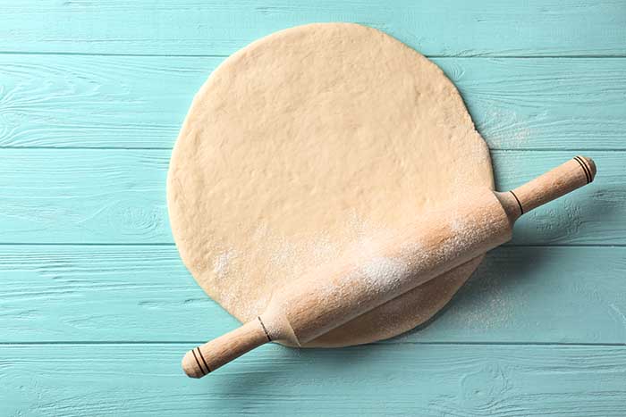 Rolling pin with dough on wooden background