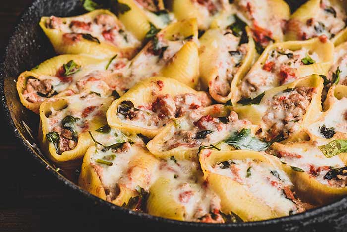 Skillet of baked jumbo shells pasta stuffed with ground beef spinach and cheese