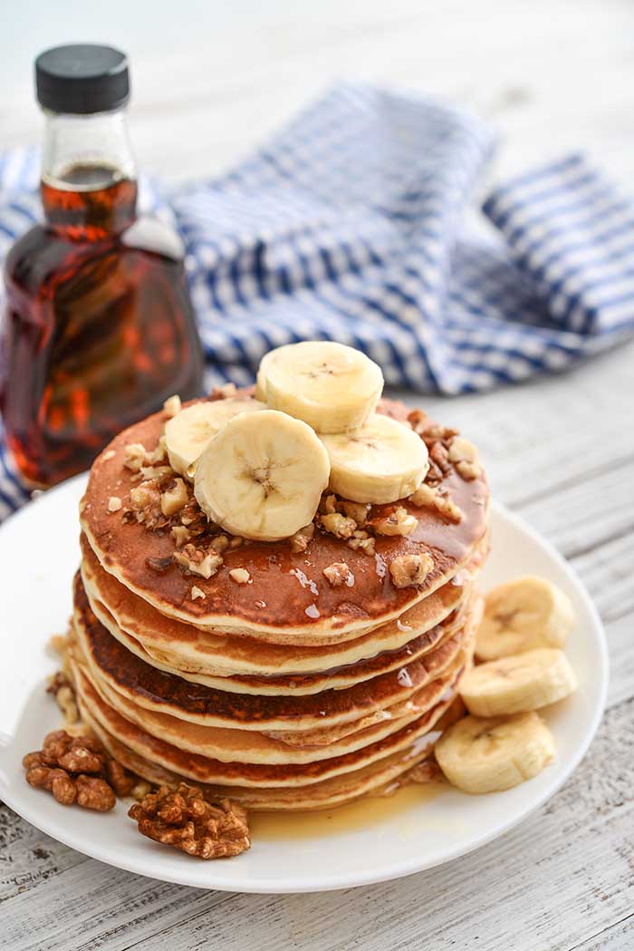 breakfast pancakes served on plate with walnuts and banana slices topped with maple syrup