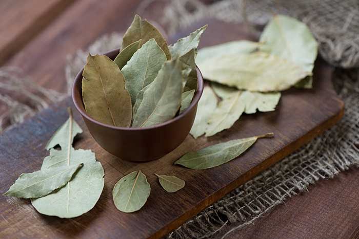 dried bay leaves in brown serving bowl on wooden cooking surface