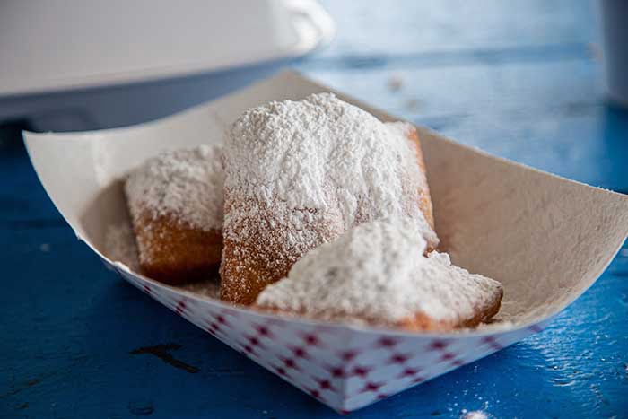 French beignets with powdered sugar on top on blue picnic table