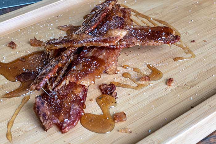 candied bacon crack served on a wooden platter with a sugary sauce.