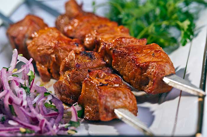 fresh portion of shish kebab on plate with onion and greens