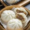 steamed chinese gluten-free bao buns resting in bamboo baozi steamer showing ground pork filling