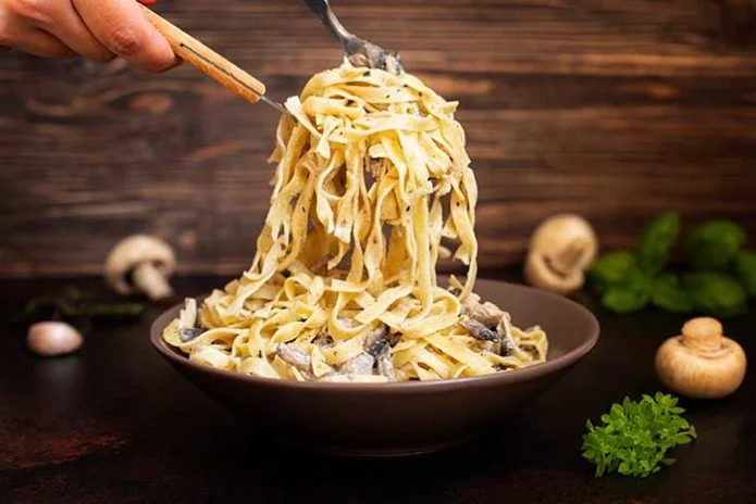 Homemade Italian fettuccine pasta with mushrooms and cream sauce (Fettuccine al Funghi Porcini). Traditional Italian cuisine. Served on a dark table with a rustic wooden background