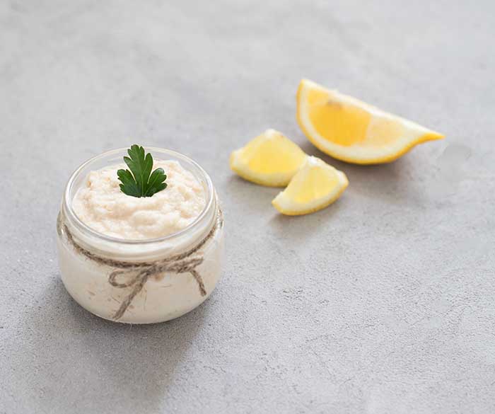 jar of white horseradish with basil and lemon slices on cooking surface