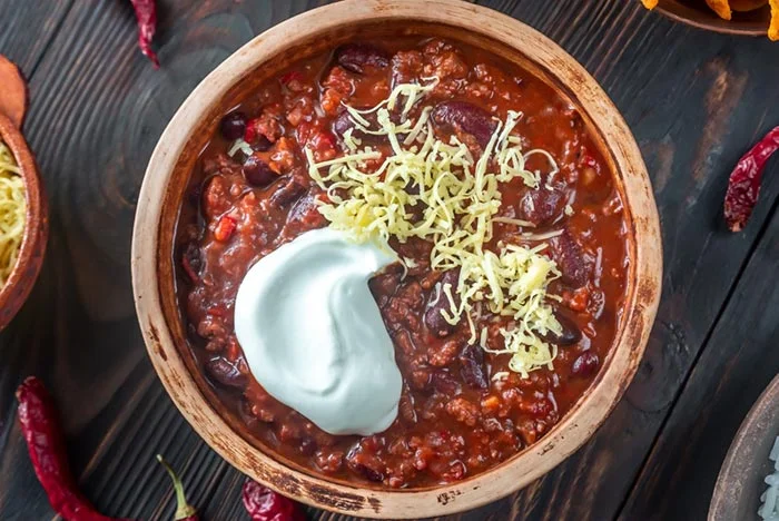 chili con carne topped with sour cream and grated cheddar cheese