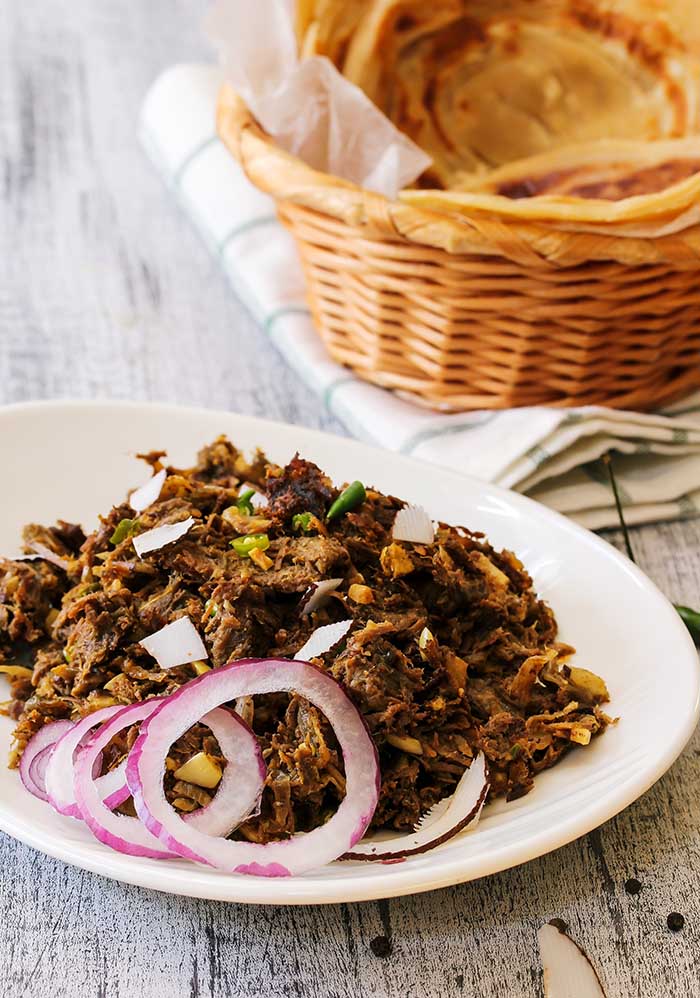 kerala beef fry served alongside indian paratha and red onion garnish