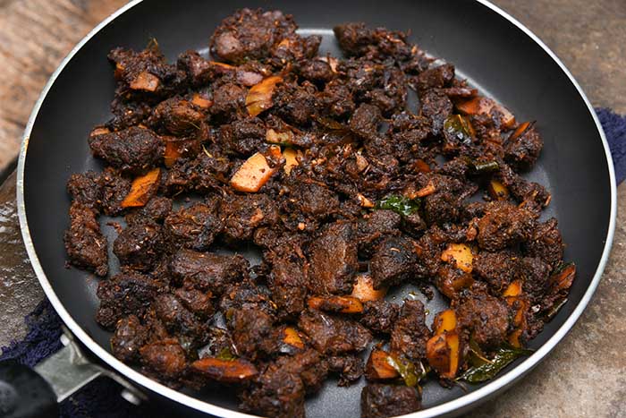 close-up of spiced beef fried in pan with curry leaves and coconut slices