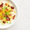 Close up of creamy potato soup with bacon and cheddar cheese in bowl on light stone