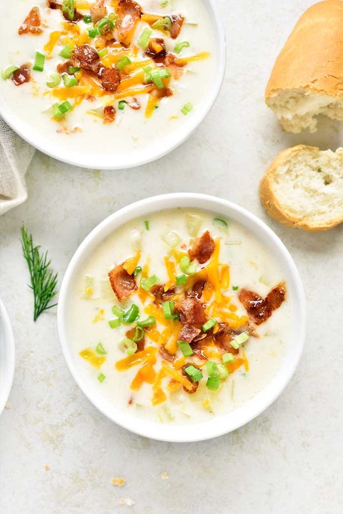 Delicious potato creamy soup with bacon and cheddar cheese in bowl on light stone