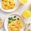 scrambled eggs presented on breakfast table with parsley garnish and orange juice