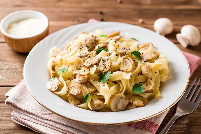 tagliatelle pasta with mushrooms, parsley and Parmesan cheese on wooden table