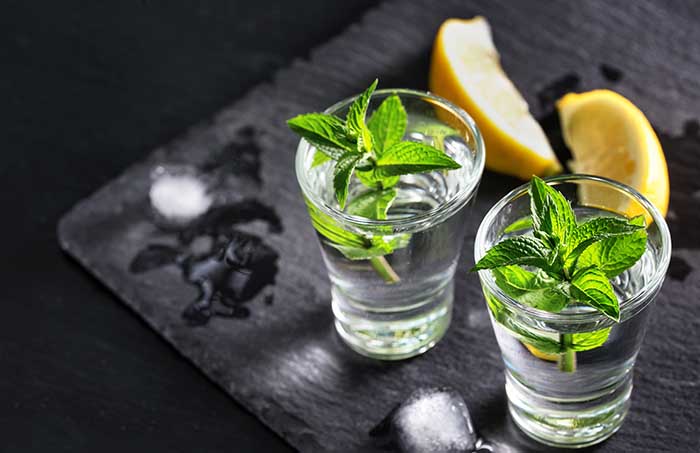 vodka with mint and ice Two glasses with a cocktail of mint and ice alcohol with lemons on the black surface